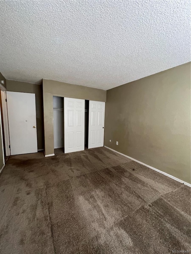 unfurnished bedroom featuring dark carpet, a textured ceiling, and multiple closets