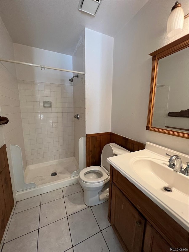 bathroom with a tile shower, tile patterned flooring, wood walls, toilet, and vanity