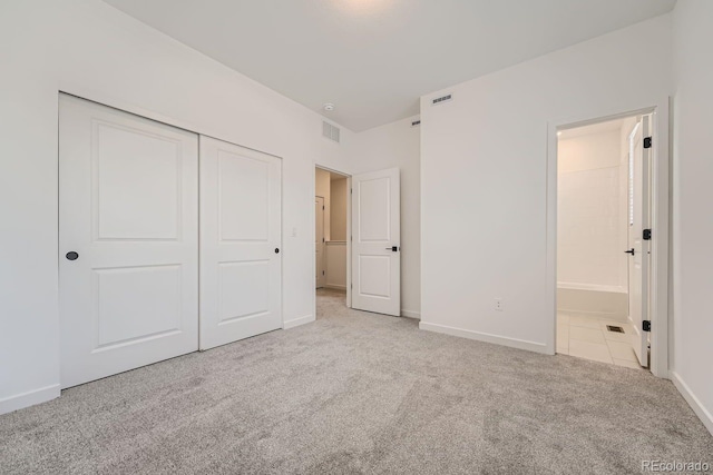 unfurnished bedroom with light carpet, ensuite bath, and a closet