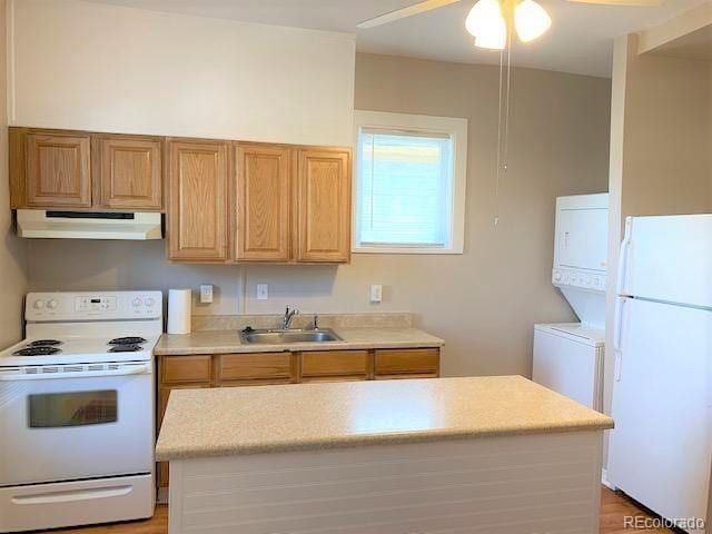 kitchen with white appliances, stacked washer and clothes dryer, sink, ceiling fan, and light hardwood / wood-style floors