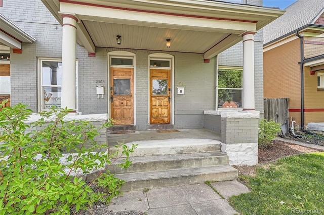 view of exterior entry with brick siding and a porch