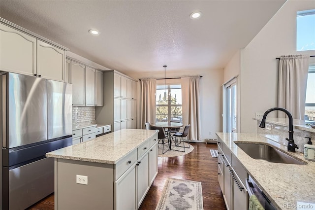 kitchen with appliances with stainless steel finishes, pendant lighting, light stone counters, a kitchen island, and sink