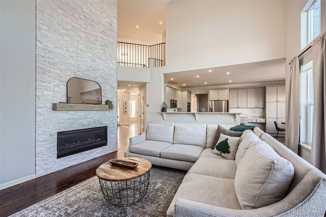 living room with a high ceiling, dark wood-type flooring, and a stone fireplace