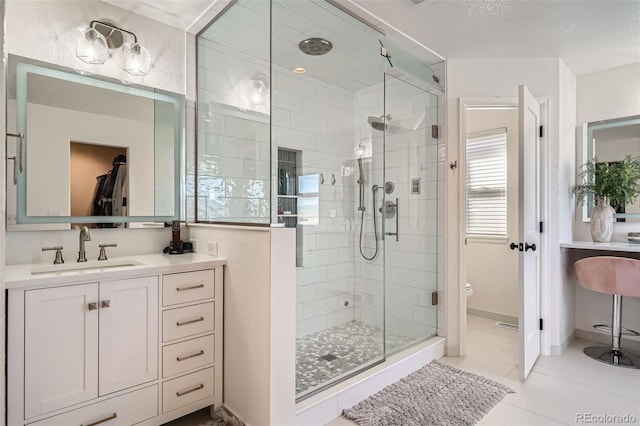 bathroom with toilet, a textured ceiling, tile patterned floors, a shower with shower door, and vanity