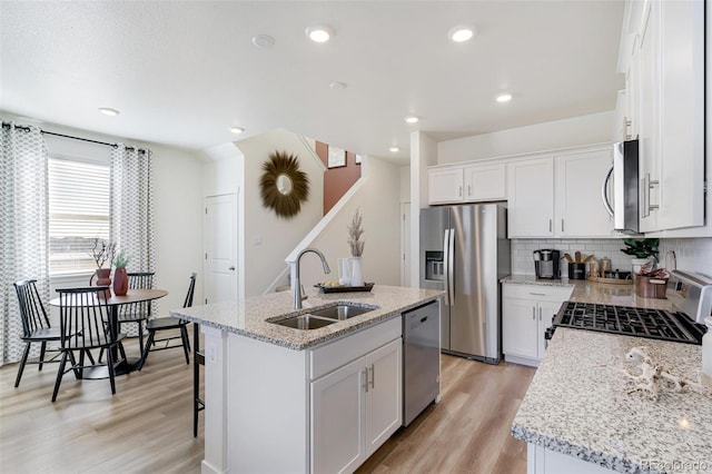 kitchen with an island with sink, a sink, light wood-style flooring, backsplash, and stainless steel appliances