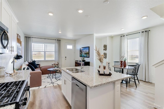 kitchen with a sink, light stone counters, white cabinets, light wood-style floors, and stainless steel appliances