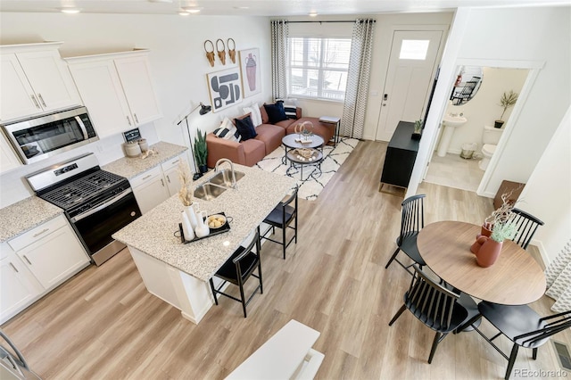 kitchen with light wood-type flooring, a sink, appliances with stainless steel finishes, and a breakfast bar