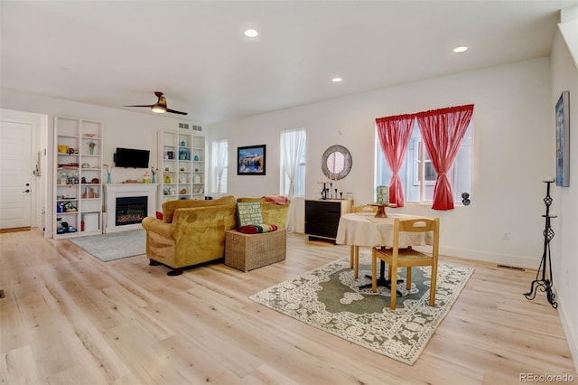 living room featuring light wood-type flooring, a glass covered fireplace, visible vents, and recessed lighting