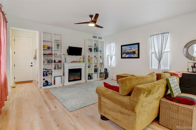 living area with light wood-type flooring, visible vents, built in features, and a glass covered fireplace