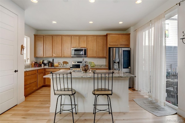 kitchen featuring light hardwood / wood-style floors, appliances with stainless steel finishes, a kitchen breakfast bar, a kitchen island, and light stone counters