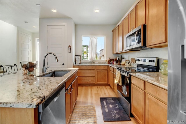 kitchen featuring light wood-type flooring, light stone countertops, appliances with stainless steel finishes, and sink