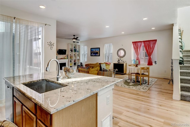 kitchen featuring open floor plan, light stone countertops, stainless steel dishwasher, a fireplace, and a sink