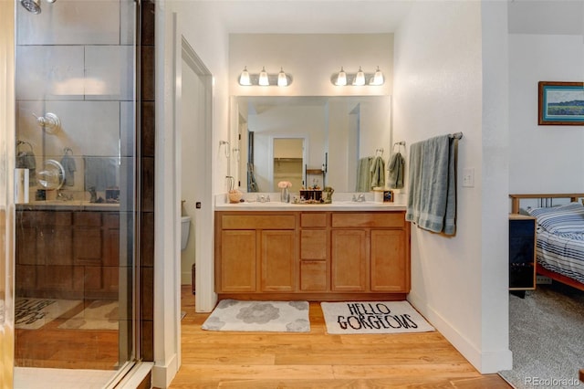 ensuite bathroom with double vanity, ensuite bath, a sink, and wood finished floors