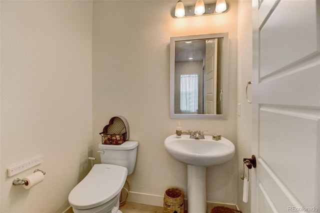 bathroom featuring toilet, baseboards, a sink, and wood finished floors