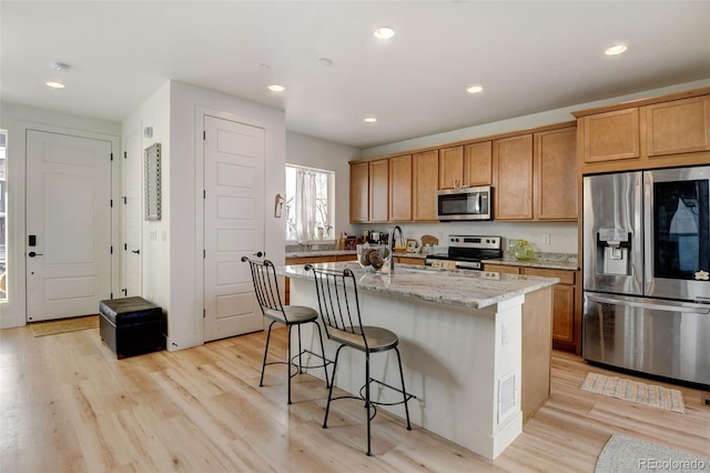 kitchen featuring light stone counters, recessed lighting, stainless steel appliances, light wood-style floors, and an island with sink