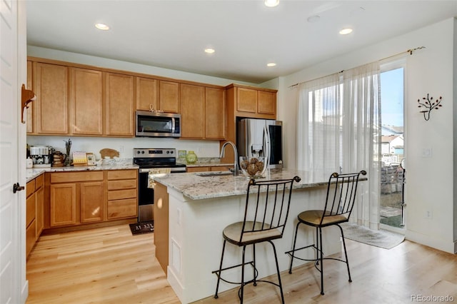 kitchen featuring light wood-type flooring, a kitchen island with sink, appliances with stainless steel finishes, and a sink