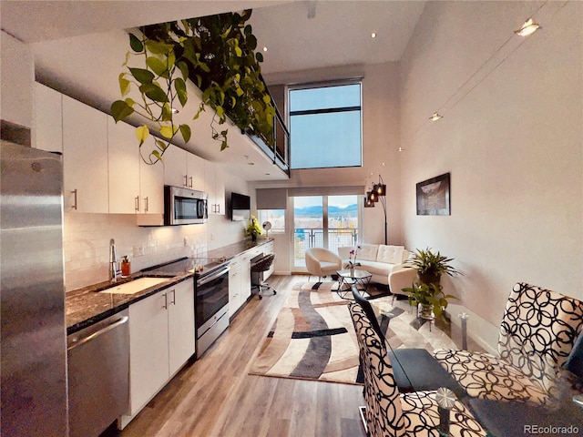 kitchen with light hardwood / wood-style flooring, high vaulted ceiling, sink, white cabinetry, and appliances with stainless steel finishes