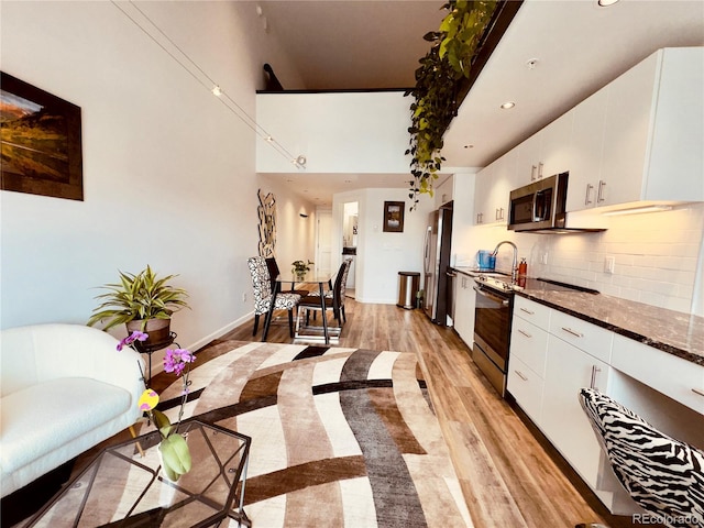 kitchen featuring white cabinetry, light hardwood / wood-style floors, stainless steel appliances, dark stone counters, and tasteful backsplash