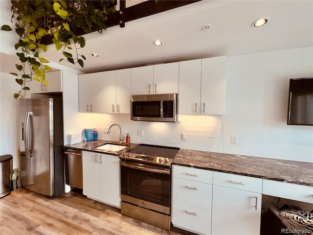 kitchen featuring light hardwood / wood-style floors, dark stone countertops, stainless steel appliances, white cabinets, and sink