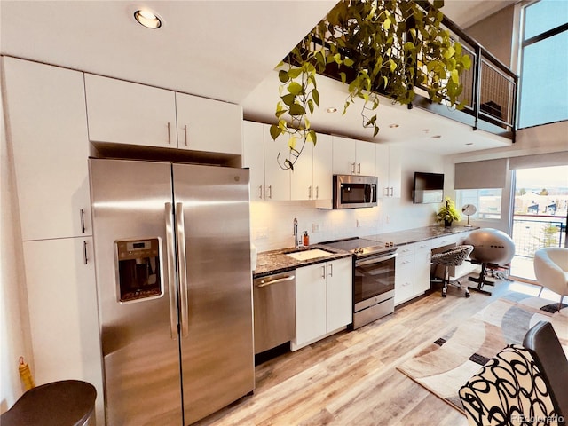 kitchen with stainless steel appliances, tasteful backsplash, light wood-type flooring, white cabinets, and sink