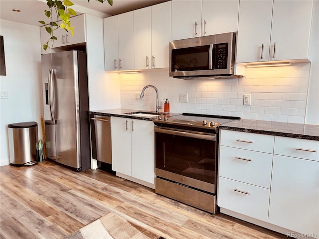 kitchen featuring light hardwood / wood-style floors, stainless steel appliances, tasteful backsplash, dark stone countertops, and white cabinets