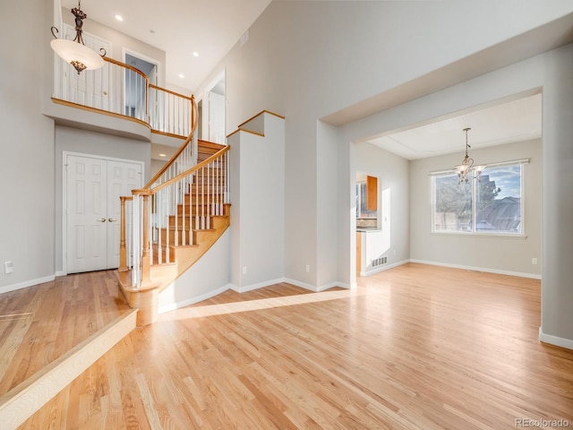 unfurnished living room with hardwood / wood-style flooring, a towering ceiling, and an inviting chandelier