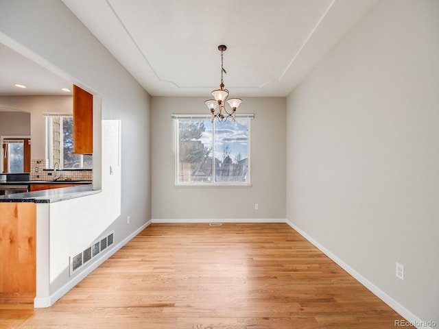 unfurnished dining area featuring sink, a chandelier, and light wood-type flooring