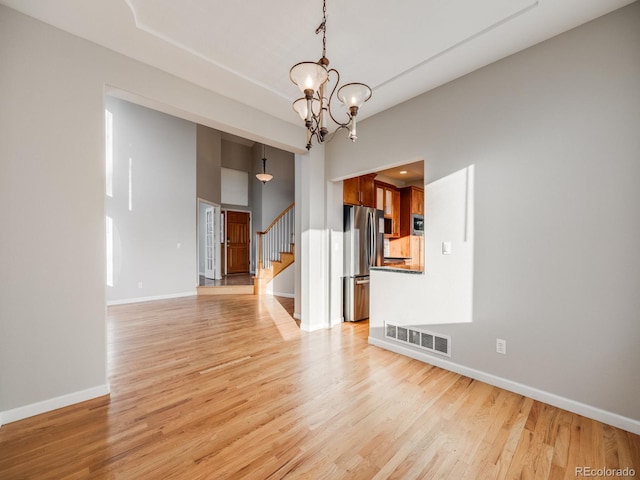 unfurnished living room featuring a towering ceiling, a notable chandelier, and light hardwood / wood-style flooring