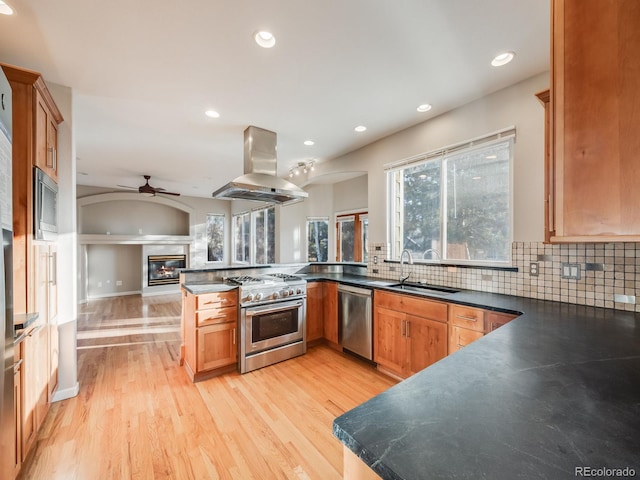 kitchen featuring sink, island range hood, kitchen peninsula, stainless steel appliances, and decorative backsplash