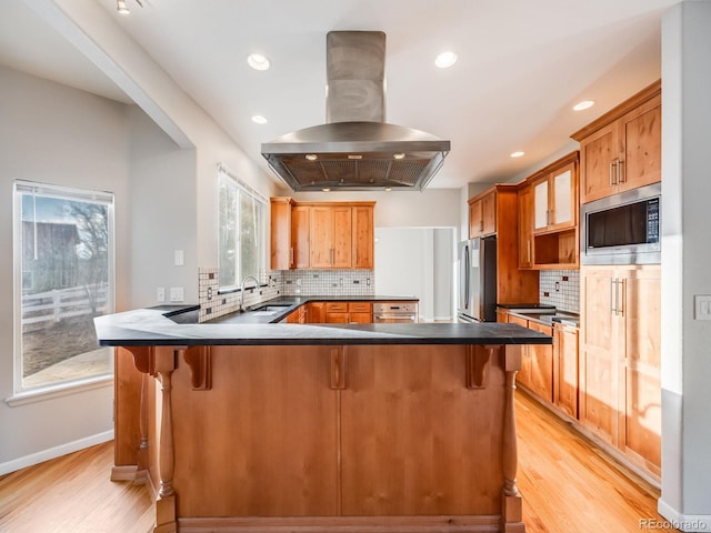 kitchen with a breakfast bar area, island range hood, light hardwood / wood-style flooring, stainless steel appliances, and backsplash