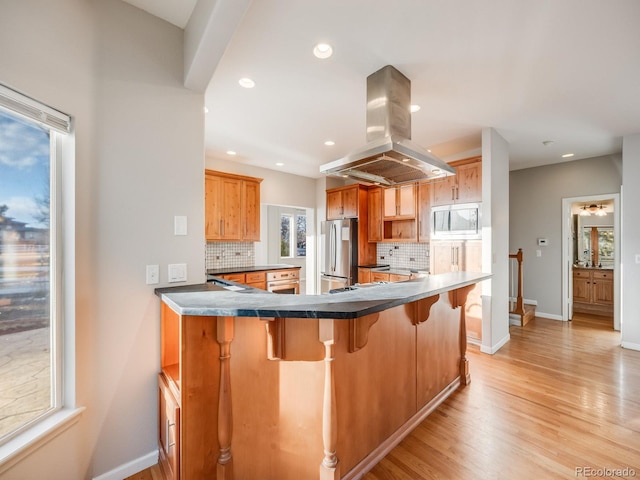 kitchen with a breakfast bar area, stainless steel appliances, island range hood, kitchen peninsula, and light wood-type flooring