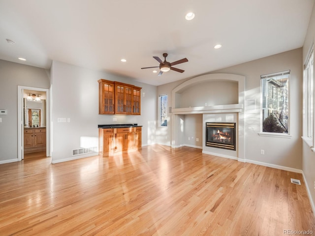 unfurnished living room with bar area, plenty of natural light, ceiling fan, and light wood-type flooring