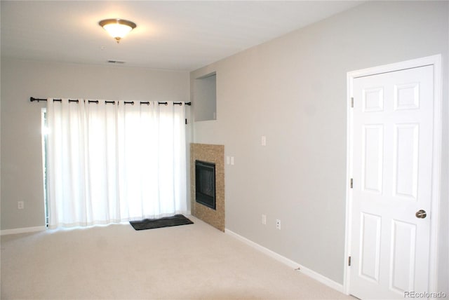 carpeted spare room with a tiled fireplace