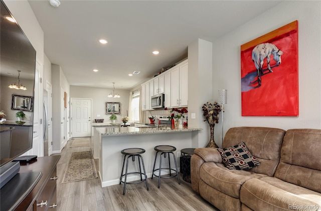 kitchen with light wood-style flooring, white cabinets, light stone counters, stainless steel appliances, and open floor plan