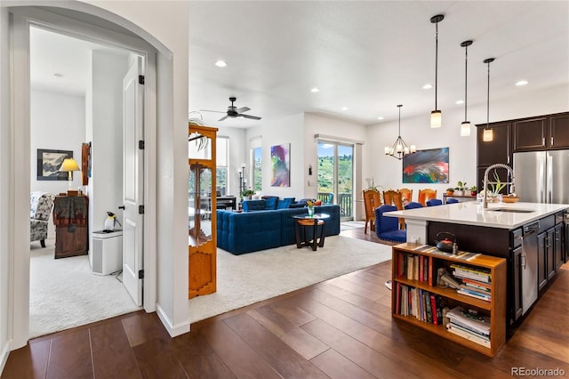 kitchen featuring dark wood-type flooring, ceiling fan with notable chandelier, sink, hanging light fixtures, and an island with sink