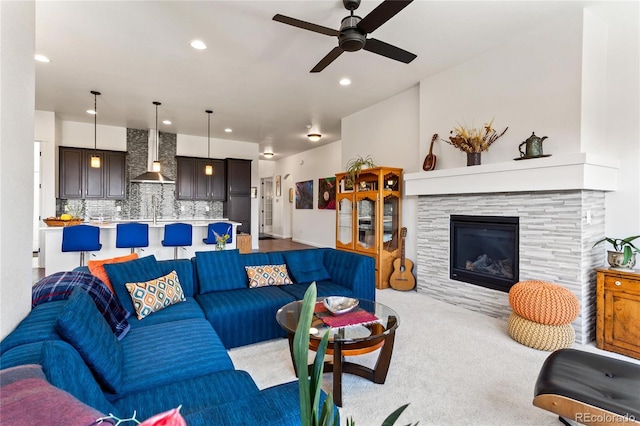 living room with sink, ceiling fan, a stone fireplace, and light carpet