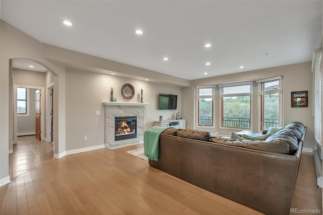 living room featuring arched walkways, baseboards, a fireplace, plenty of natural light, and recessed lighting