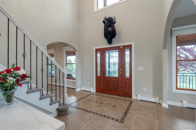 tiled entrance foyer with a baseboard radiator, a baseboard heating unit, plenty of natural light, and a towering ceiling