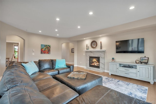 living area with arched walkways, recessed lighting, light wood finished floors, baseboards, and a premium fireplace