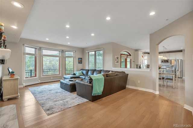 living room featuring baseboard heating, arched walkways, light wood-style floors, recessed lighting, and baseboards