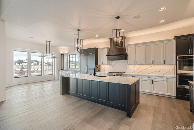 kitchen featuring decorative light fixtures, sink, decorative backsplash, a kitchen island with sink, and custom range hood