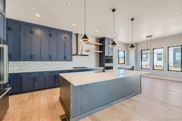 kitchen featuring wall chimney range hood, decorative light fixtures, sink, and blue cabinets