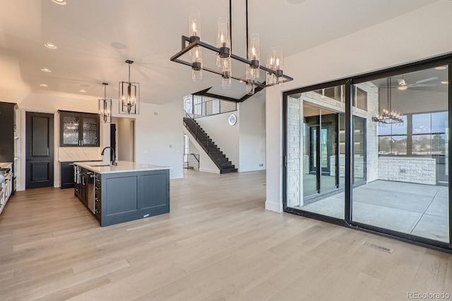 kitchen with sink, hanging light fixtures, a notable chandelier, a center island with sink, and light hardwood / wood-style flooring