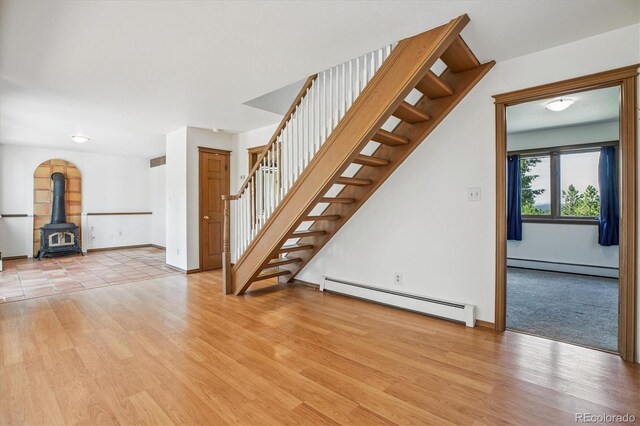 5939 S Skyline Dr, Evergreen, CO 80439 - unfurnished living room featuring baseboard heating, light wood-style flooring, stairs, and a wood stove