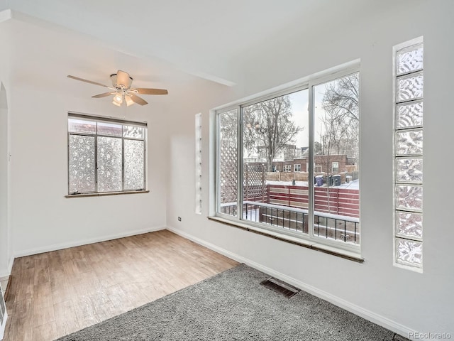 empty room featuring a wealth of natural light, ceiling fan, and hardwood / wood-style floors