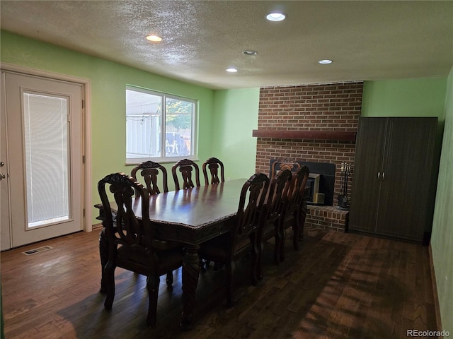 dining area with a brick fireplace, a textured ceiling, and dark hardwood / wood-style flooring