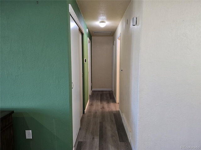 corridor with a textured ceiling and dark wood-type flooring