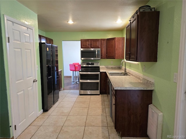 kitchen featuring stainless steel appliances, dark brown cabinetry, light tile patterned floors, and sink