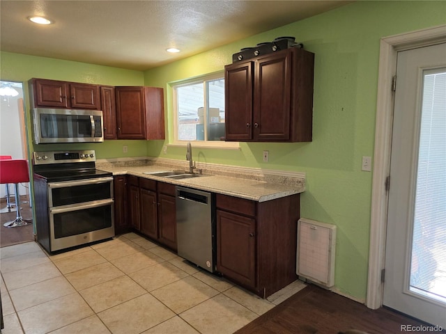 kitchen with dark brown cabinetry, light tile patterned floors, stainless steel appliances, and sink