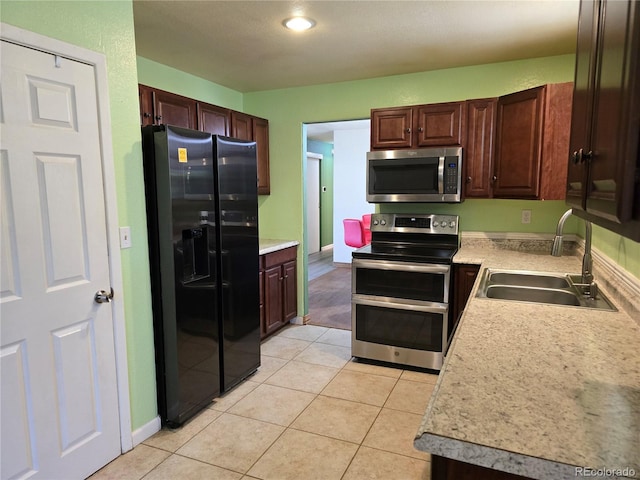 kitchen featuring dark brown cabinetry, sink, light tile patterned floors, and stainless steel appliances